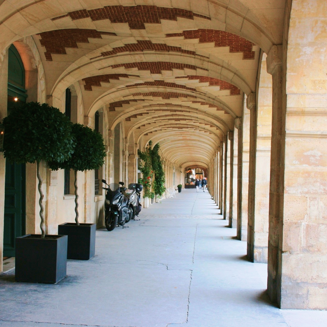 Sous les arcades en brique et pierre de la Place des Vosges.